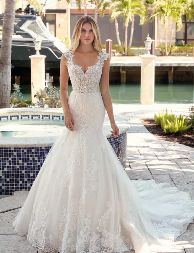 Blonde Braut in Brautkleid Meerjungfrau mit Träger in Blumenmuster mit Wasser und Palmen im Hintergrund Rückenansicht mit Schulterblick