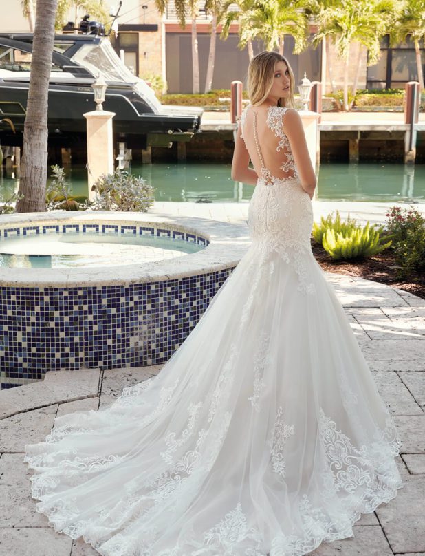 Blonde Braut in Brautkleid Meerjungfrau mit Knopfleiste und Träger in Tattoo Optik mit Wasser und Palmen im Hintergrund Rückenansicht mit Schulterblick