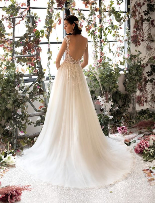 Schwarzhaarige Braut in Brautkleid Vintage ärmellos mit Träger mit geschlossenen Augen in Raum mit weißen und rosanen Blumen sowie Blättern Rückenansicht