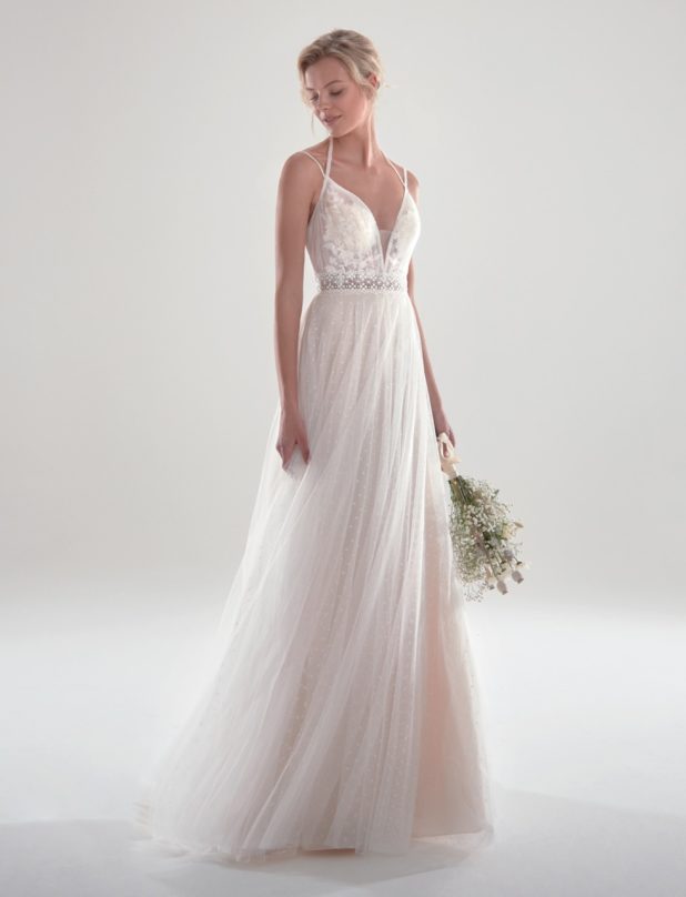 Blonde Braut in Brautkleid A-Linie Vintage mit Spaghettiträger ärmellos mit Strauß in der Hand und Blick auf den Boden Schulterblick vor grauem Hintergrund