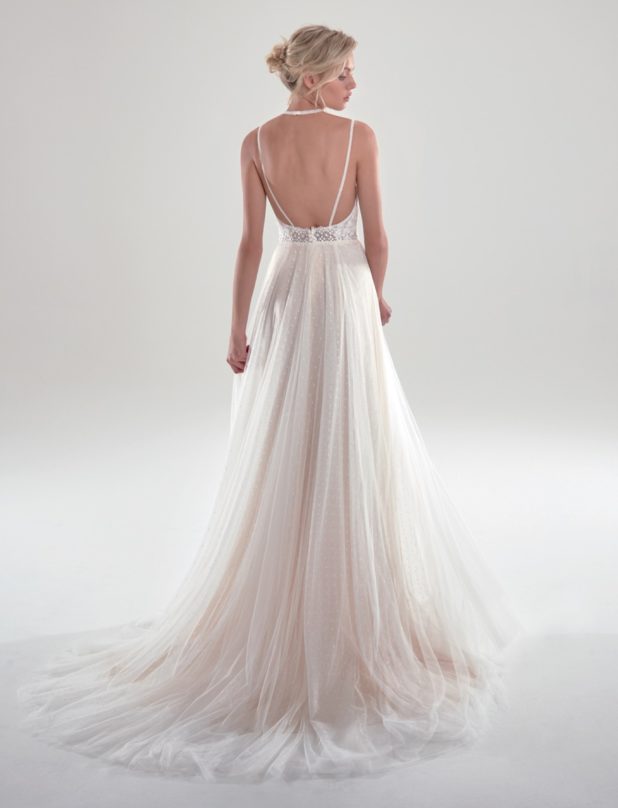 Blonde Braut in A-Linien Brautkleid mit langem Spaghettiträger und ärmellos vor grauem Hintergrund mit Blick auf den Boden Seitenansicht Fotostudio