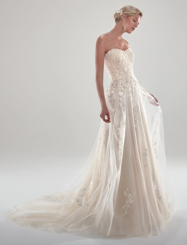 Blonde Braut in A-Linien Brautkleid trägerlos und ärmellos vor grauem Hintergrund Fotostudio Seitenansicht