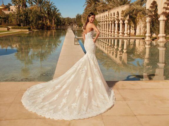 Brünette Braut in Brautkleid Fit & Flare vor einem Weg zwischen Wasser im Garten eines Palasts in Rückenansicht mit Schulterblick