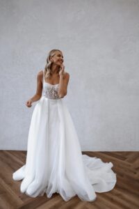 Braut in A-Linien-Brautkleid mit transparentem Spitzenoberteil und fließendem Tüllrock, lächelnd.