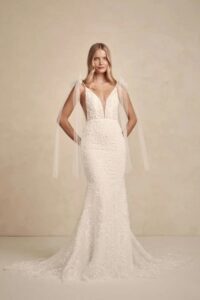 Frontansicht eines romantischen Brautkleides mit tiefem V-Ausschnitt, zarten Trägern mit Tüllschleifen und figurbetonter Silhouette.
