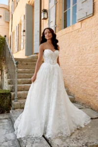 Romantisches A-Linien-Brautkleid mit Spitze und fließendem Rock, getragen vor einer stilvollen Treppe im warmen Tageslicht.