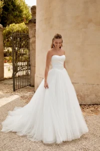 Braut in cleanem A-Linie Brautkleid mit voluminösem Rock und romantischer Schleppe in stilvoller Outdoor-Kulisse.