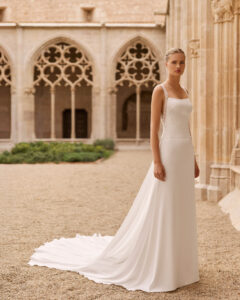 Elegantes Brautkleid in gerader Silhouette mit eckigem Ausschnitt, filigranen Spitzenträgern, schmaler Spitzenbordüre an der Taille und langer Schleppe im historischen Innenhof.