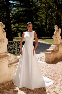 Brautkleid im A-Linien-Schnitt aus mattem Satin mit Bateau-Ausschnitt, Taschen und langer Schleppe, Ganzkörperansicht vor barocker Gartentreppe mit Skulpturen.