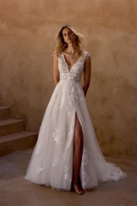Brautkleid im A-Linien-Schnitt mit tiefem V-Ausschnitt, transparentem Spitzenoberteil, Beinschlitz und fließendem Tüllrock mit floralen Applikationen, Frontalansicht.