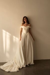 Braut in einem luxuriösen Prinzessinnen-Brautkleid aus Satin mit schulterfreiem Drapé-Ausschnitt, geformter Korsage und weitem Rock in minimalistischer Kulisse.