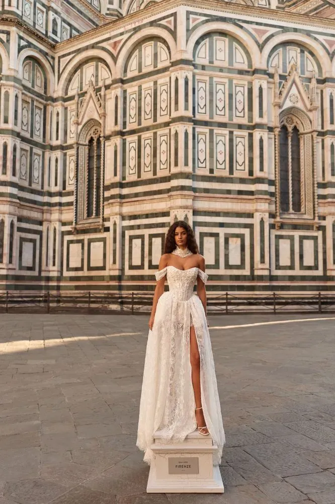 Braut in Brautkleid mit Carmen-Ausschnitt, Spitzen-Choker und durchgehender Chantilly-Spitze vor Domfassade.